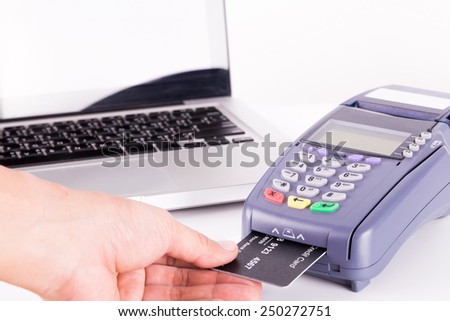 Human Hand Swiping Credit Card Machine with Laptop In Background