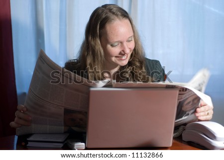 A woman sitting and smiling while reading the morning paper.