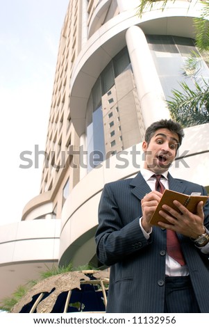 A business man, in gray suit, planning his day, with a building in the background.