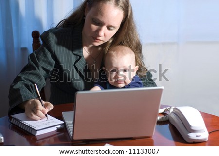 A woman writing in her day planner while holding her son.
