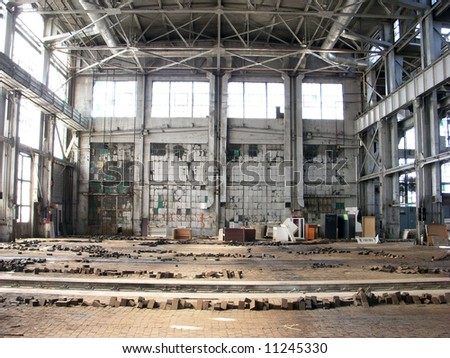 An indoor shot of a large and abandoned factory, with light streaming in from tall leaded glass windows.