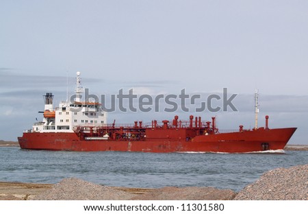 Large red ship steaming through a narrow channel