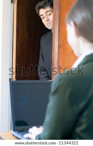 Man in business attire nosing around a doorway into a room where a female colleague is working
