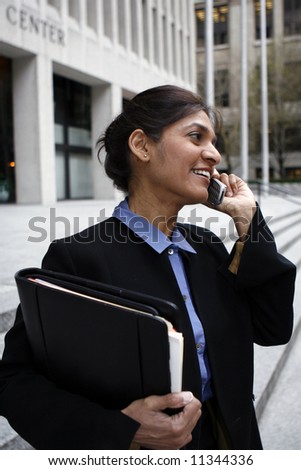 Executive Indian woman talking on a cellphone dressed in a black suit.