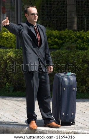 Latin american businessman in a suit waiting on the curb with his luggage with his arm out to flag someone down