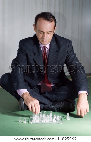 A businessman in a suit, sitting on the floor cross-legged, playing with chess pieces.