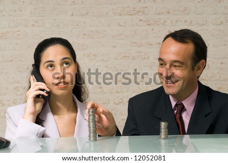 Businessman reaching over and stealing money playfully from his female colleague while she talks on the phone