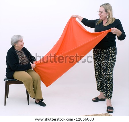 Woman and her elderly mother folding a piece of orange fabric. Isolated against a white background