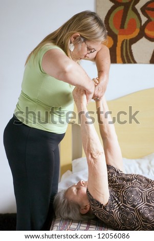 Woman helping her elderly mother with stretches and physical therapy exercises