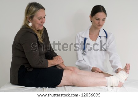 Younger female doctor wrapping a bandage around the ankle of an older female patient. Isolated.