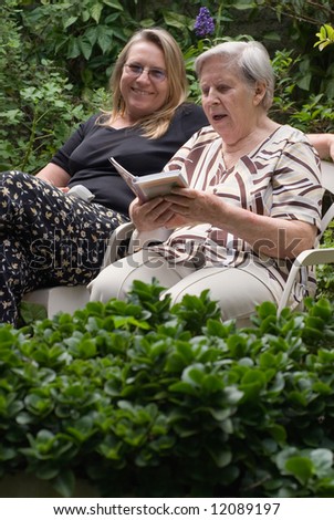 Latin american woman and her elderly mother reading together in a lush green garden