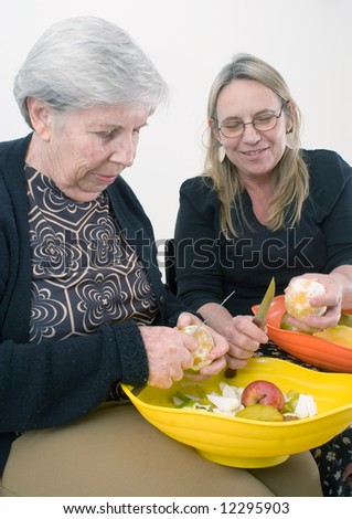 Adult woman and her older mother peeling fruit together. Isolated