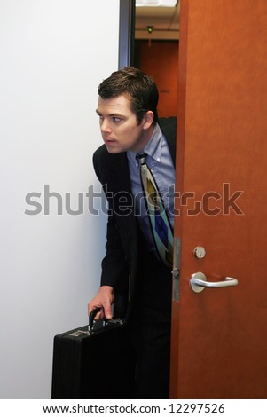 A shot of businessman peaking his head out of a door to see if he can sneak out the office.