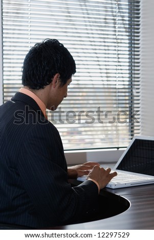 Silhouette of a businessman sitting on a laptop by a window