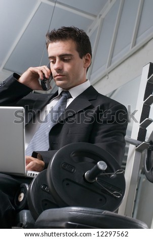 Businessman in the gym working on his cell phone and laptop