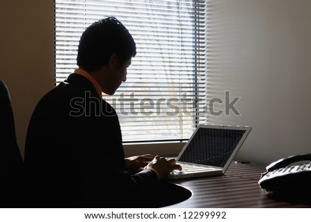 Silhouette of a businessman sitting on a laptop by a window