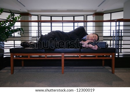 Man in a business suit asleep on a couch in an office hallway