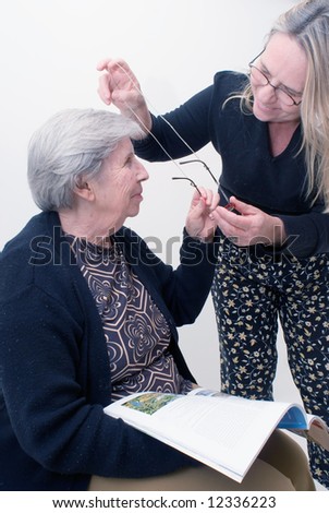 An isolated shot of a adult child putting glasses on her elderly mother.