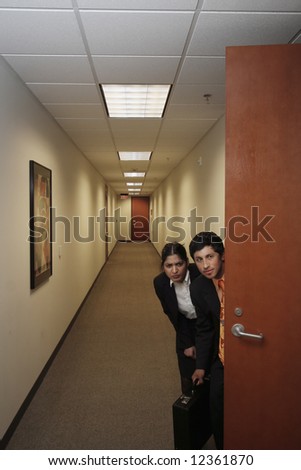 A shot of a businessman and businesswoman sneaking out of an office.