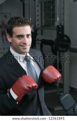 A shot of a businessman, in a suit, wearing a pair of boxing gloves.