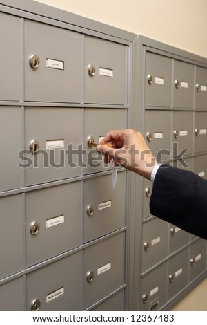Close up of a hand putting a key into a lock in a row of mailboxes or safety deposit boxes