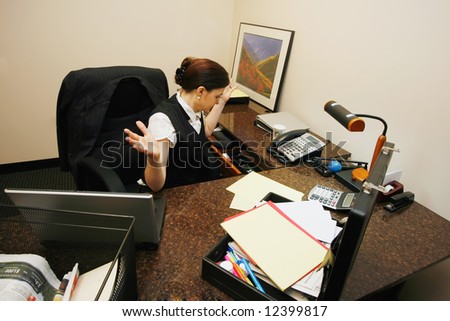 Businesswoman sitting at her desk with her hands in the air as she searches for something