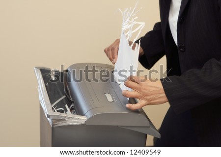 Close-up of a woman shredding a piece of paper in an office shredder