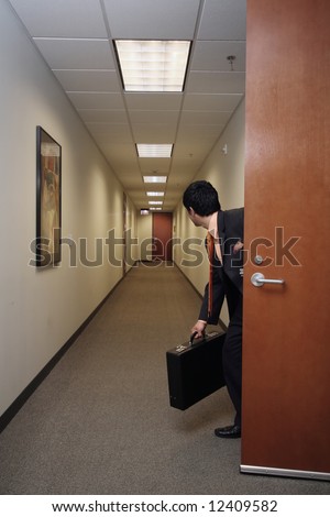 Businessman looking around suspiciously with his briefcase in hand in an empty hallway