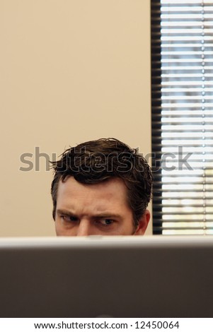Businessman sitting behind his laptop with an angry look on his face. Vertically framed shot.