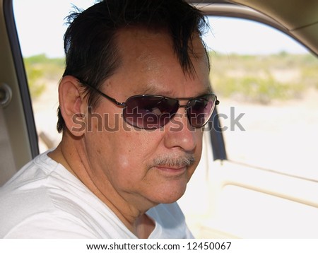 An isolated shot of an older man driving a SUV in the desert, wearing sunglasses.