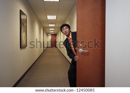 Young businessman peering into an empty hallway through a doorway