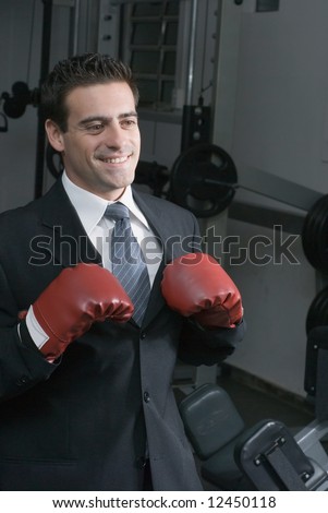 Confident attractive man in a business suit and wearing boxing gloves. Shot is set in a gym and he has a big smile on his face