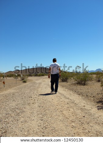 A shot of a older man walking in the desert in a white t-shirt.