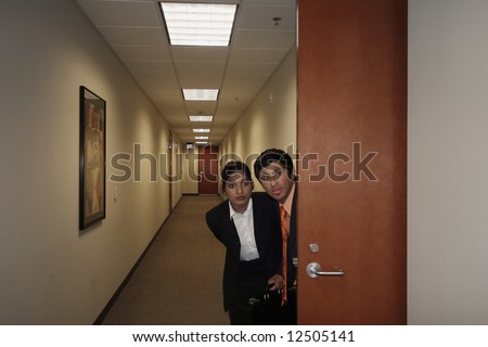 A shot of a businessman and businesswoman sneaking out of an office. Both looking in the same direction.