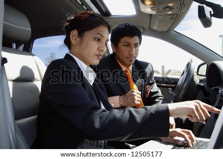 Business colleagues reviewing something on a laptop while seated in a car on a sunny day