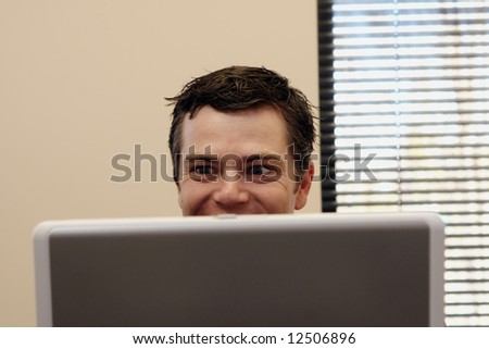 Businessman sitting behind a laptop smiling as he reads the screen. Horizontally framed shot.
