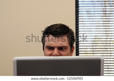 Businessman behind a laptop screen with an angry look on his face. Horizontally framed shot