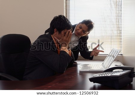 Female boss dressing down a younger male subordinate while pointing a finger at his laptop screen