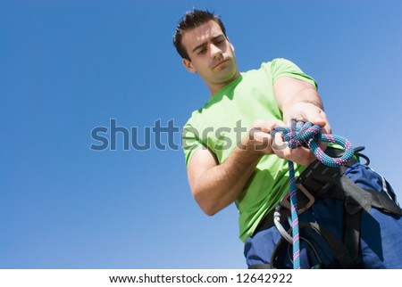 Attractive, fit young man tying a knot in a climbing rope. Set against a clear blue sky