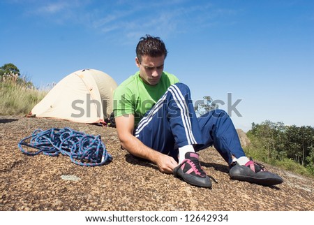 Attractive young man putting on his rock-climbing shoes in front of his tent