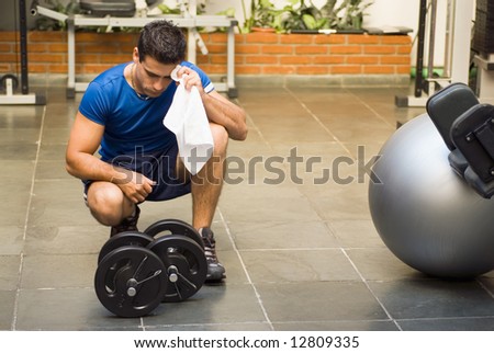 Male athlete kneeling down by dumbbells toweling sweat of his brow.