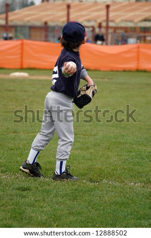 Young boy in baseball uniform winding up to throw the ball back to the mound. Vertically framed shot.