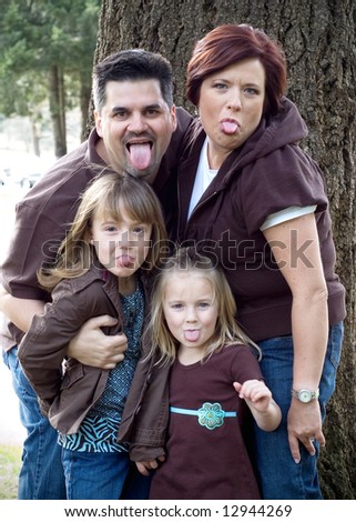 Cute family of four sticking their tongue out at the camera. Vertically framed shot.