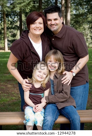 Family of four huddled together in a park on a sunny day. Vertically framed shot.