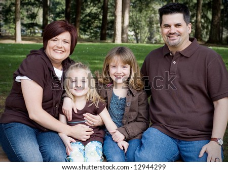 Family of four sitting together on a park bench. Horizontally framed shot.