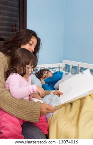 Mother reading her children bedtime stories. Her daughter is sitting on her lap and her son is lying in bed.