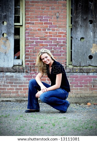 Attractive blond woman crouching down in front of an old brick building. Vertically framed shot