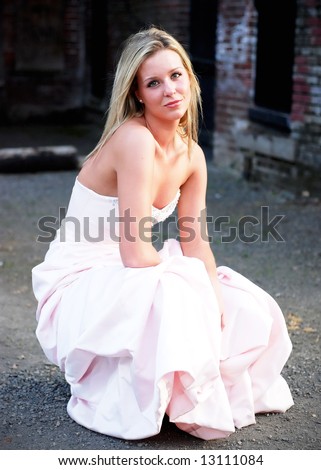 Attractive blond woman kneeling down in a bridesmaid\'s dress. Vertically framed shot.