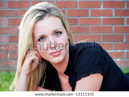 Attractive blond woman crouching down in front of an old brick building. Horizontally framed close-up shot