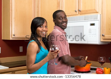 Attractive young African American couple cooking dinner together and drinking red wine.  Horizontally framed shot with the man and woman looking towards the camera.